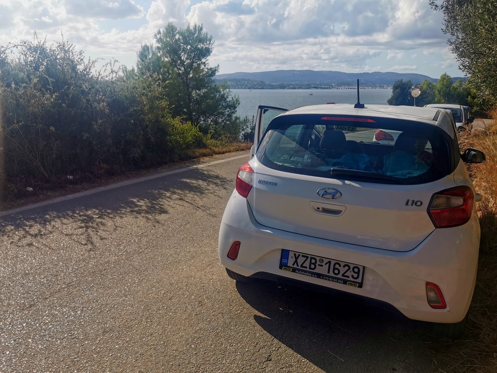 Ein weißes Auto, das am Meer in Griechenland geparkt ist.