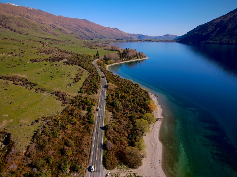 Straße zwischen blauem See und grünen Hügeln in Neuseeland
