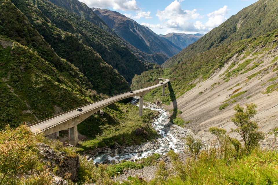Autos auf dem geschwungenen Otira-Viadukt über einem steinigen Fluss in den Bergen am Arthur's Pass, Neuseeland.